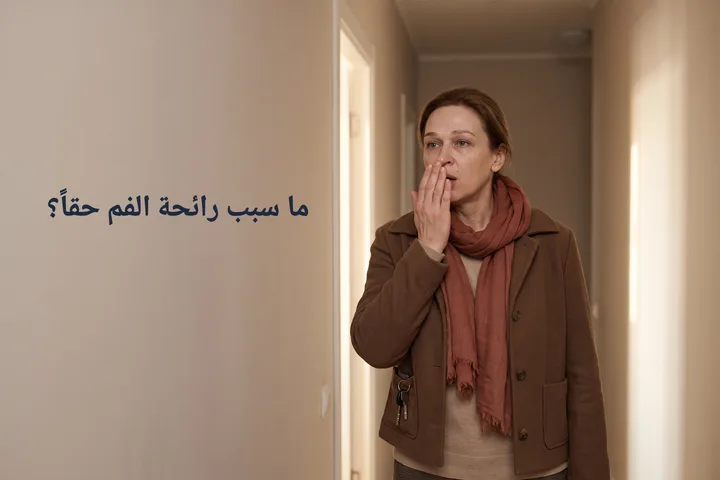ما سبب رائحة الفم حقاً؟ — امرأة عند باب بيتها تنفخ في راحة يدها المقوسة