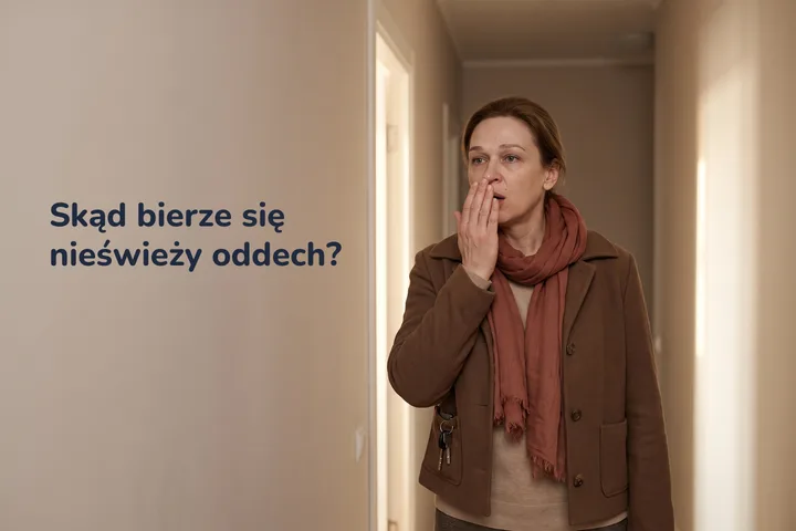 Skąd bierze się nieświeży oddech? — kobieta przy własnych drzwiach wejściowych chucha w złożoną dłoń