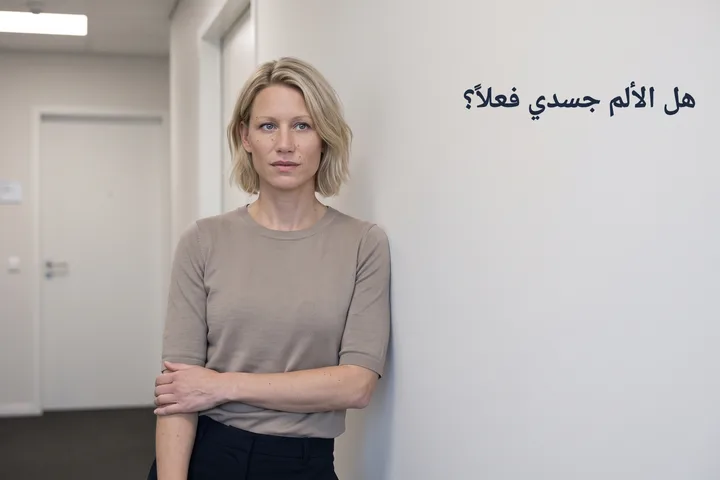 هل الألم جسدي فعلاً؟ — امرأة تتوقف في ممر مكتب وساعدها مضغوط على وسط بطنها