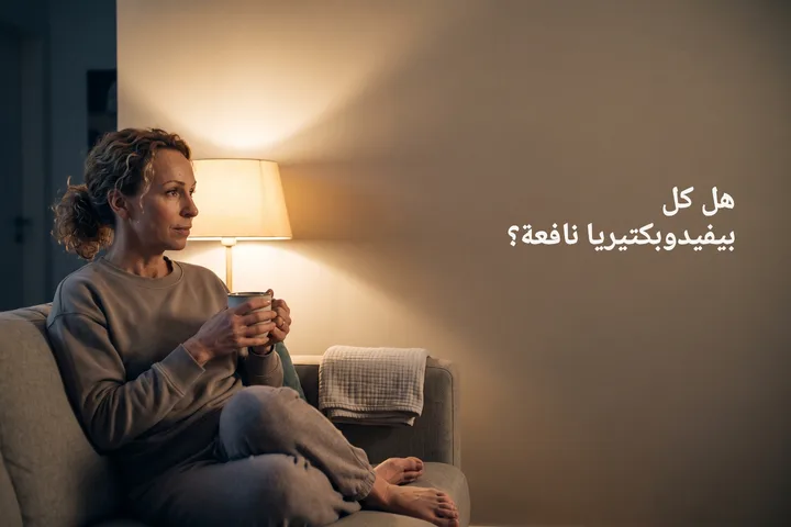 هل كل بيفيدوبكتيريا نافعة؟ — امرأة في أواخر العشرينيات تجلس على الأريكة وبيدها كوب في ضوء مصباح