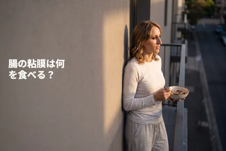 腸の粘膜は何を食べる？ — 20代の女性が最後の日ざしの中、バルコニーでオートミールを食べている