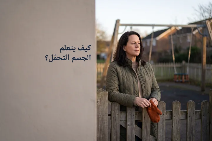 كيف يتعلم الجسم التحمّل؟ — امرأة تتوقف عند بوابة ملعب أطفال خالٍ في شمس العصر المنخفضة