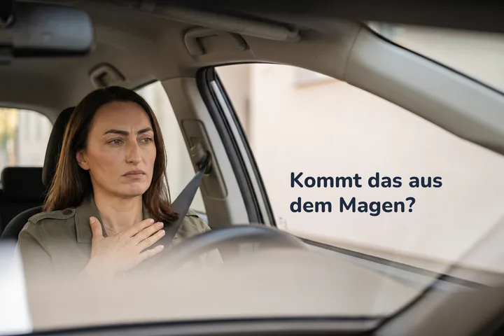Kommt das aus dem Magen? — eine Frau vormittags in ihrem geparkten Auto, die Handfläche flach auf dem Bauch