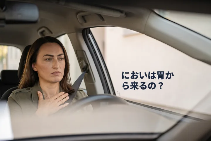 においは胃から来るの? — 午前なかば、停めた車の中で女性が手のひらをおなかに当てている