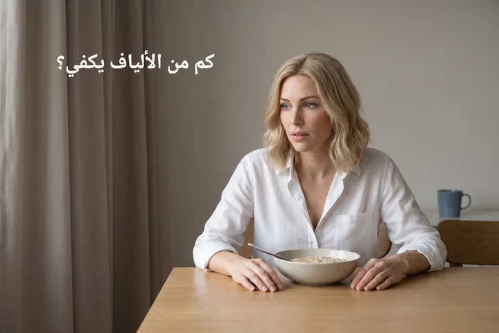 كم من الألياف يكفي؟ — امرأة إلى طاولة الطعام في أول الصباح، أمامها صحن عصيدة شوفان